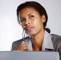 Contemplative young businesswoman holding a spectacles while using laptop